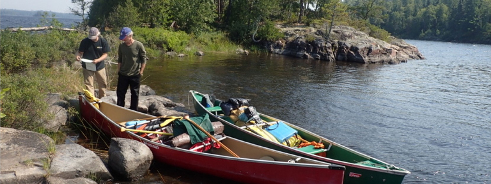 2 men look at a map standing near their canoes.