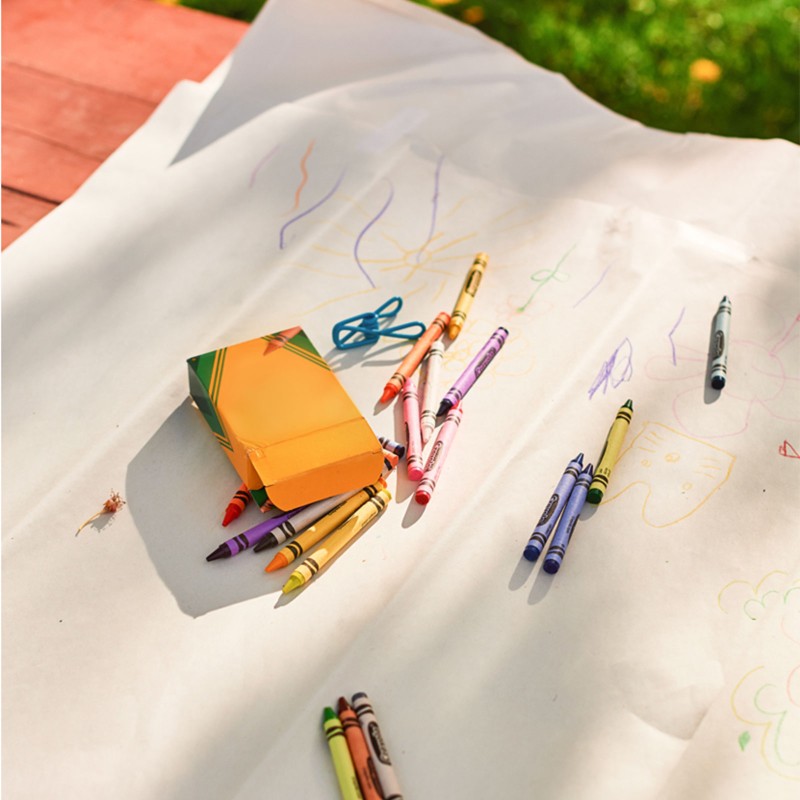 An outdoor picnic table with large pieces of newsprint and crayons on it.