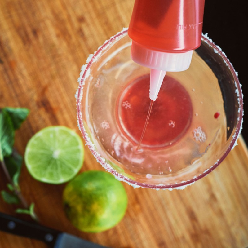 Someone squeezing a beautiful pink liquid into a sugar rimmed margarita glass.