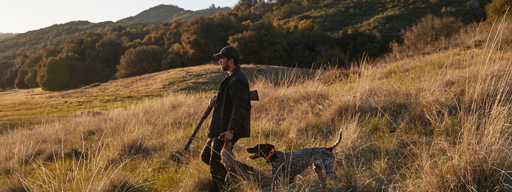 A hunter walking through a field with a dog.