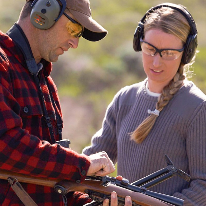 Two hunters, one demonstrating loading a rifle, both wearing ear protection.