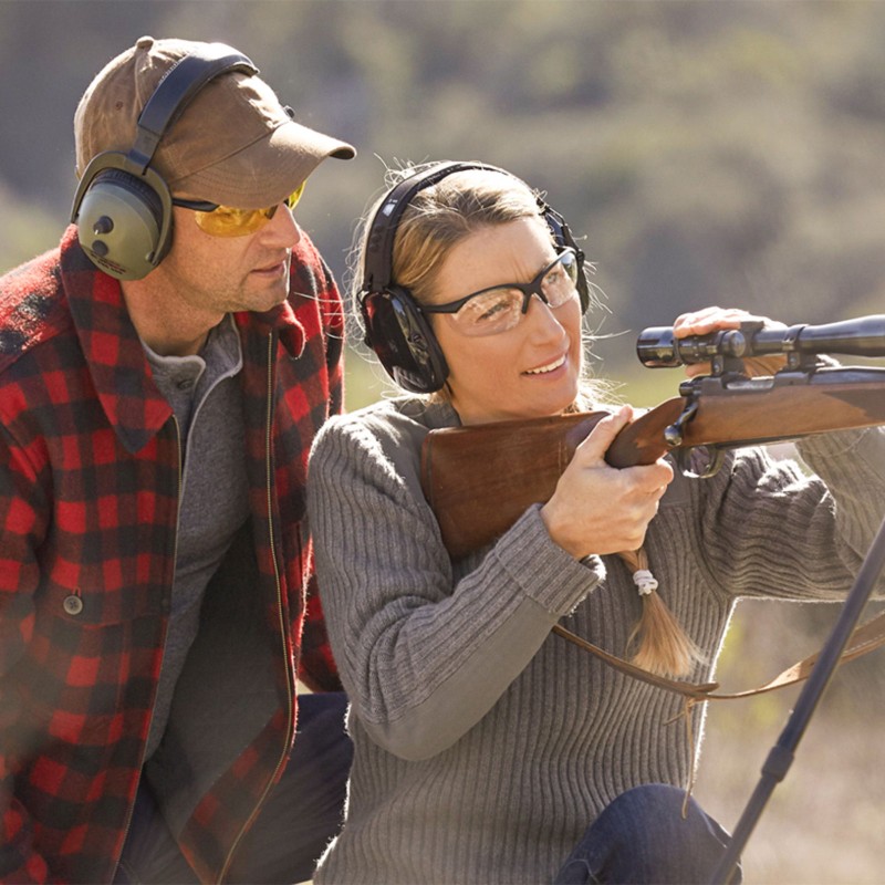 2 hunters, one instructing while the other looks through the scope of her rifle.