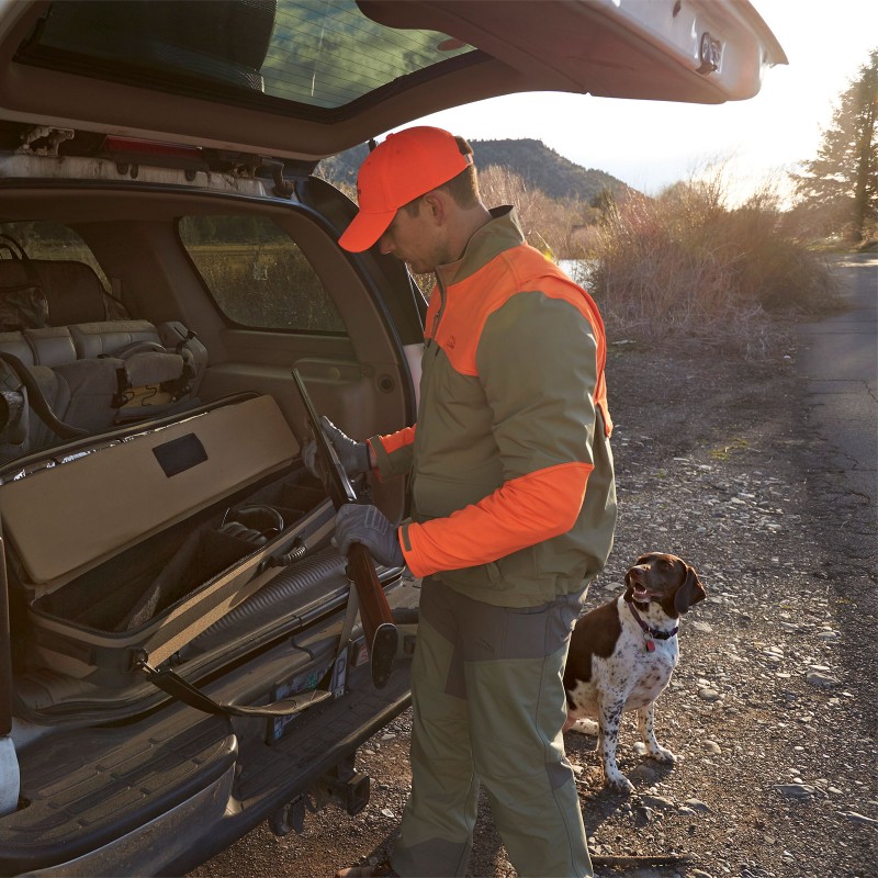 A hunter getting a rifle from the trunk of his vehicle, dog by his side.