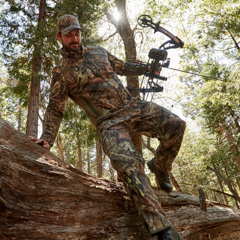 A bow hunter climbing over a large downed tree.