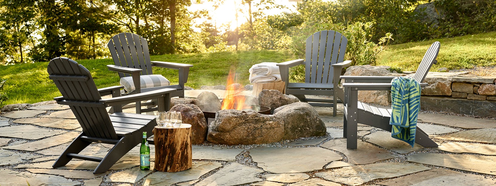 Beautiful backyard patio scene with adirondack chairs around a firepit, sun setting in the background.