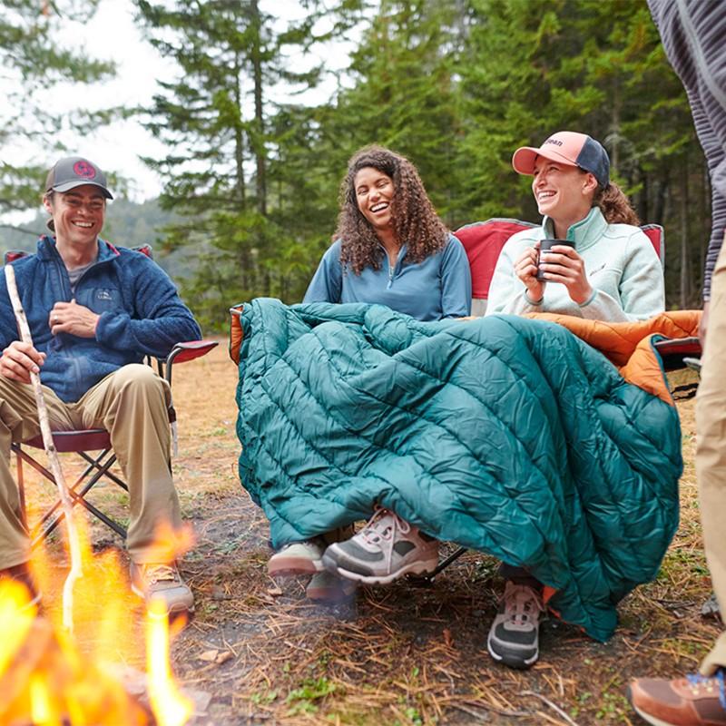 Smiling friends sitting in camp chairs around a campfire.