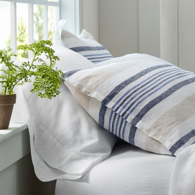 Close-up of plain and striped linen sheets on a cozy bed.