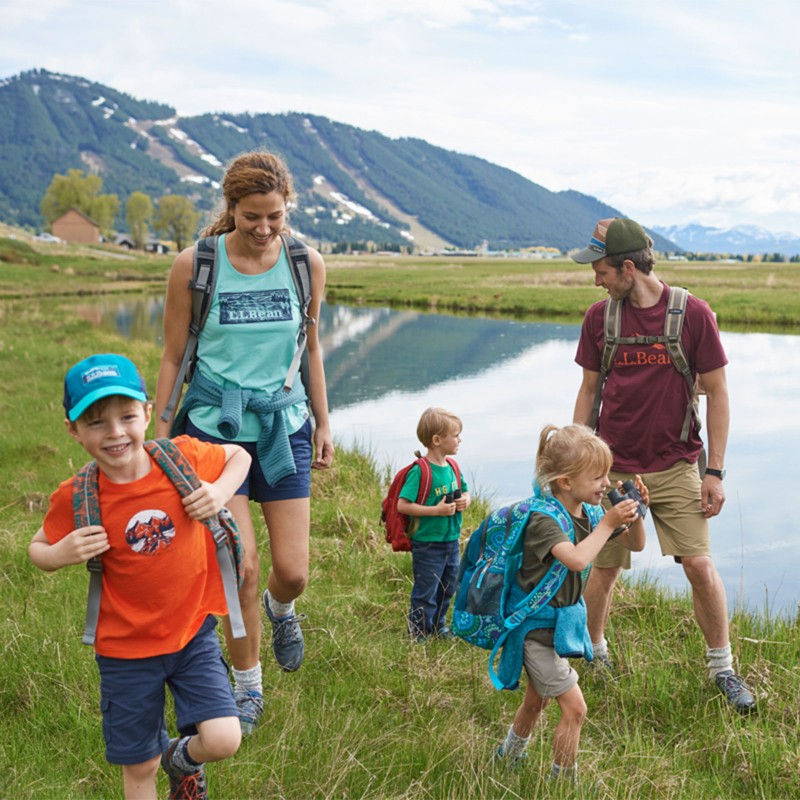 A family hiking in a field by a river, mountains in the background.