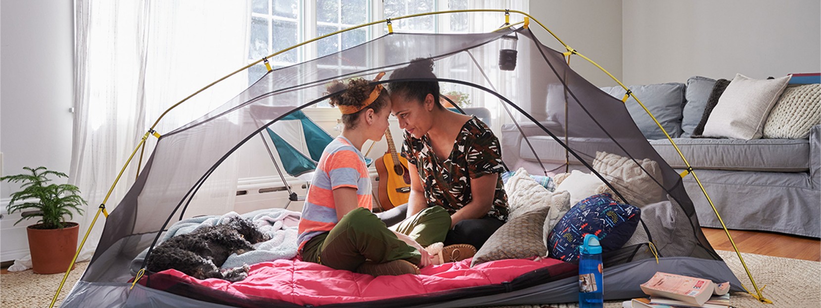 Mom and child sitting in a tent in their living room, indoor camping.