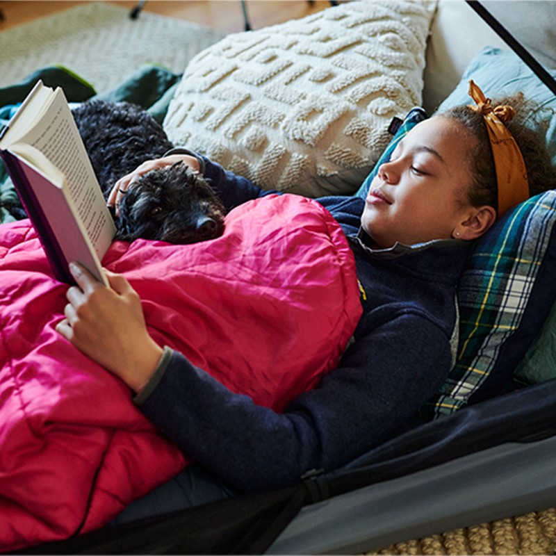 Child in a sleeping bag laying inside a tent reading.