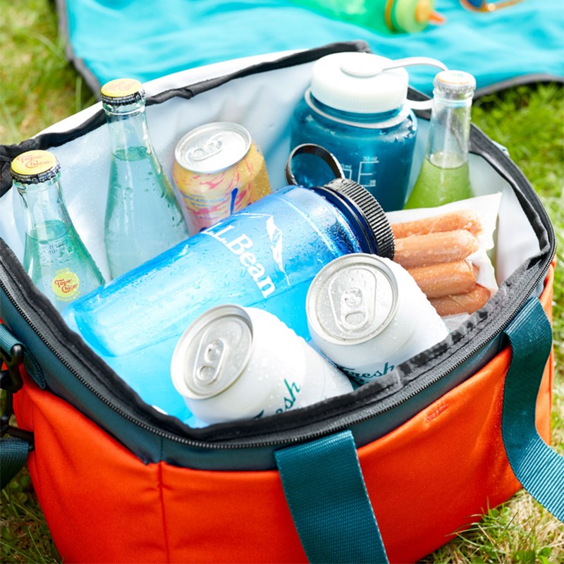 A soft-sided cooler on the grass filled with drinks, hot dogs and half-frozen water bottles.