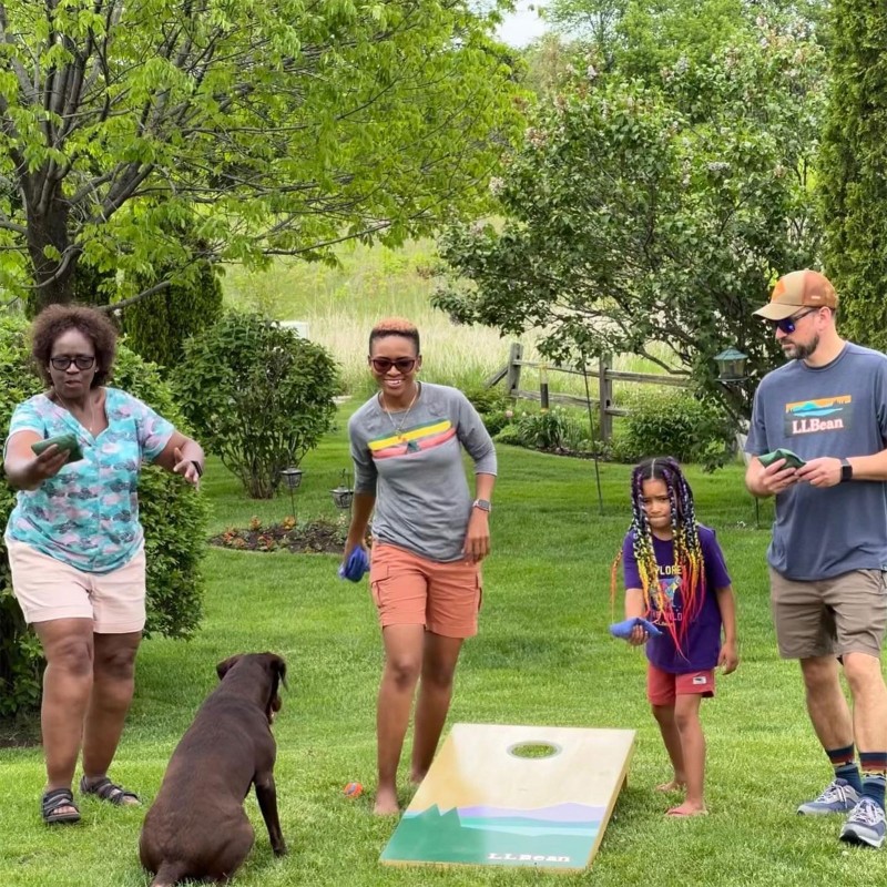 4 people playing cornhole while a dog looks on.