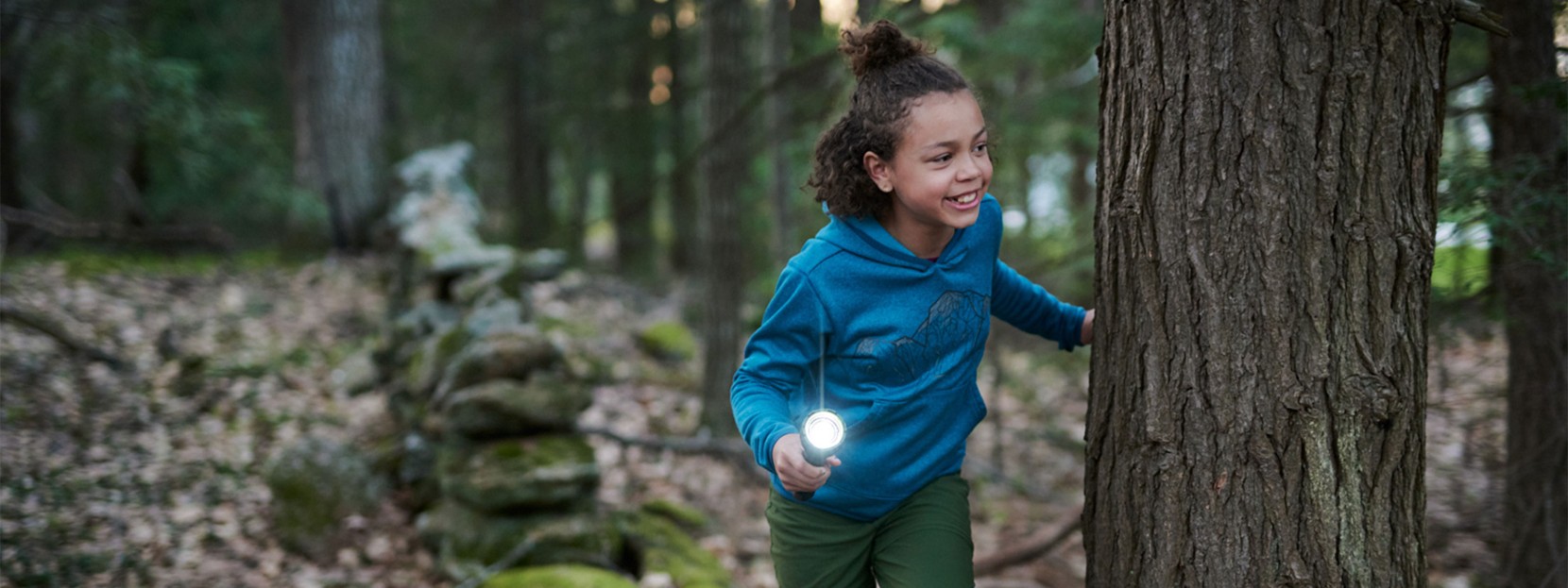A young girl peaks around a tree with a flashlight playing flashlight tag.
