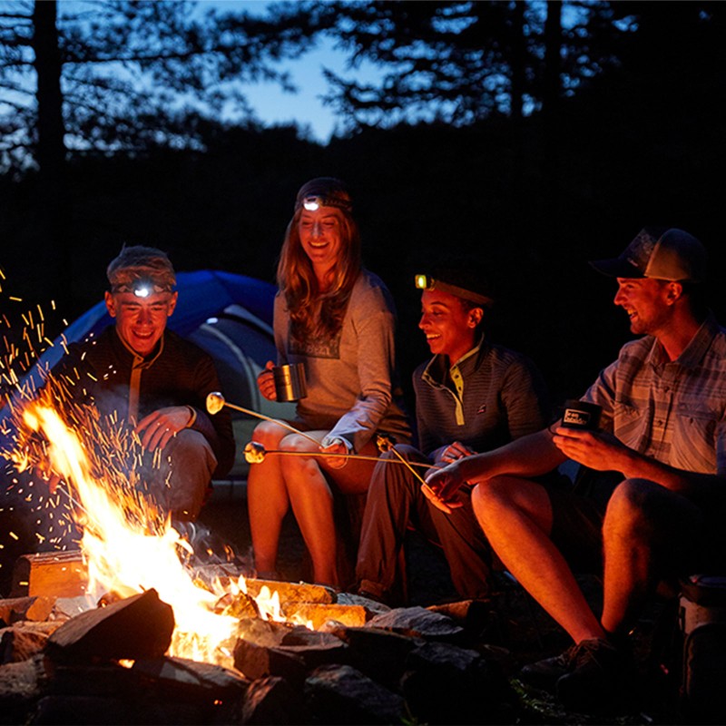 Friends wearing headlamps toasting marshmallows around a campfire