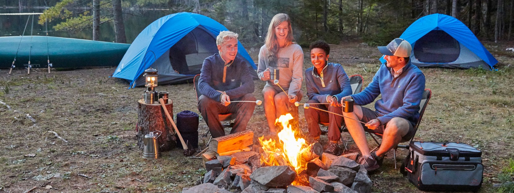 A family sitting around a campfire, tents in the background.