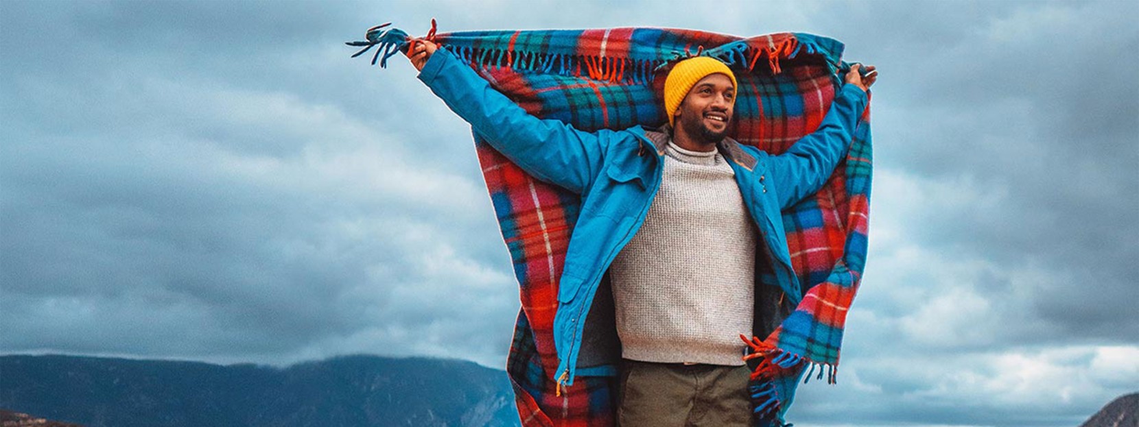 Joshua Walker holding up a fluttering plaid blanket, mountains all around.