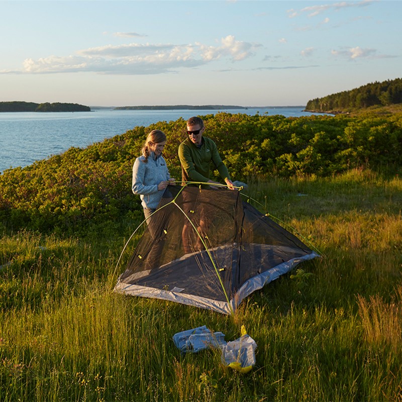 A couple setting up a tent on an island, a canoe in the foreground.