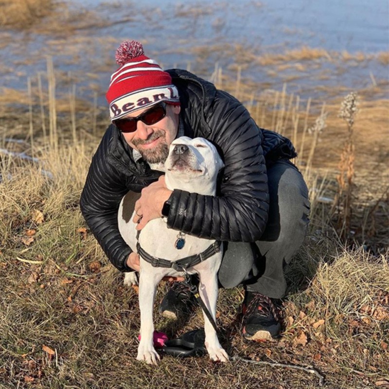 Dan Tarkinson outside, scootching down hugging a dog.