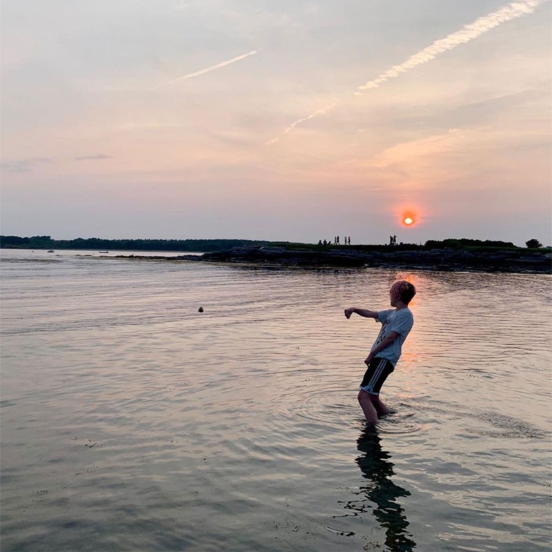 Dan Tarkinson throwing a rock in the water as the sun sets behind him.