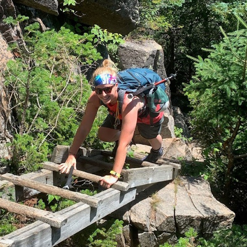 Amy C. with full day pack, climbing a wooden ladder on a steep section of a trail.