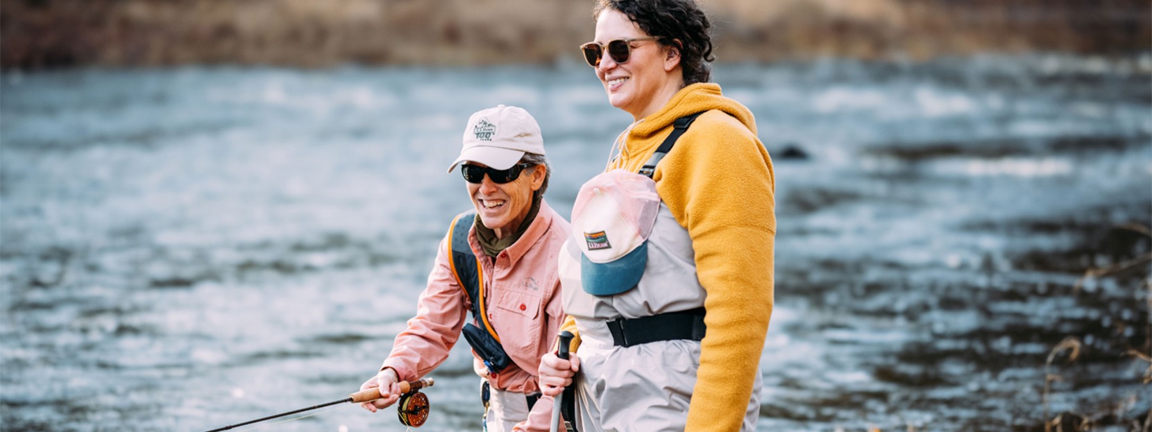 Julie M. standing in a stream watching her fly-fishing instructor Sue cast.