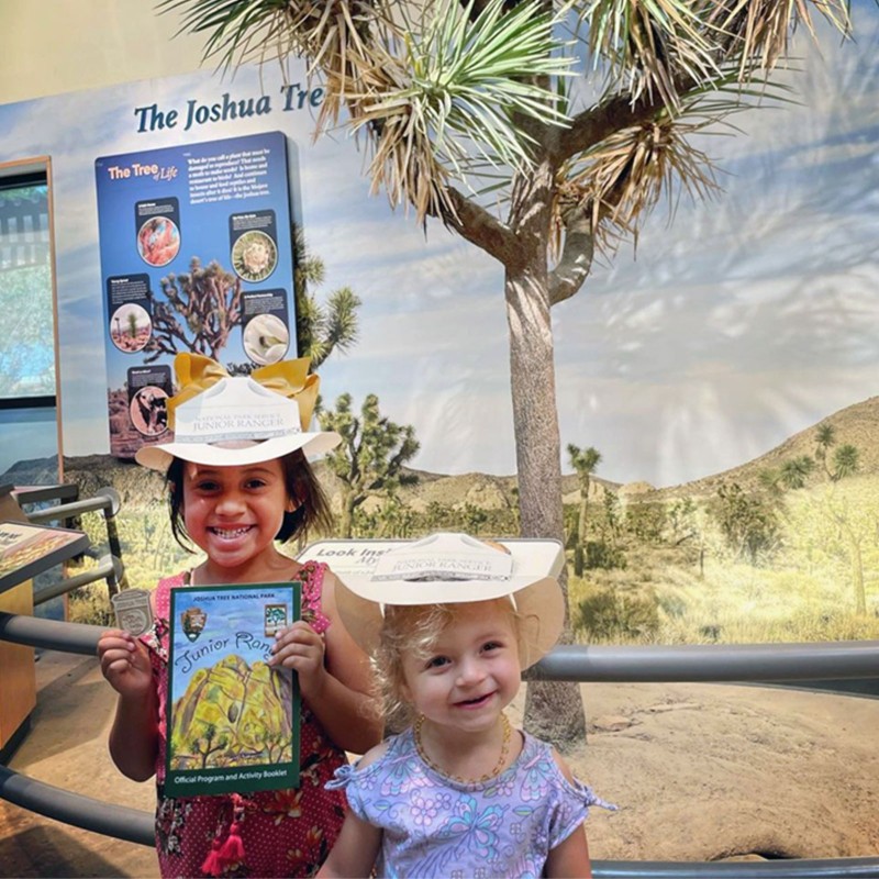 Smiling children holding a Joshua Tree Junior Ranger booklet.