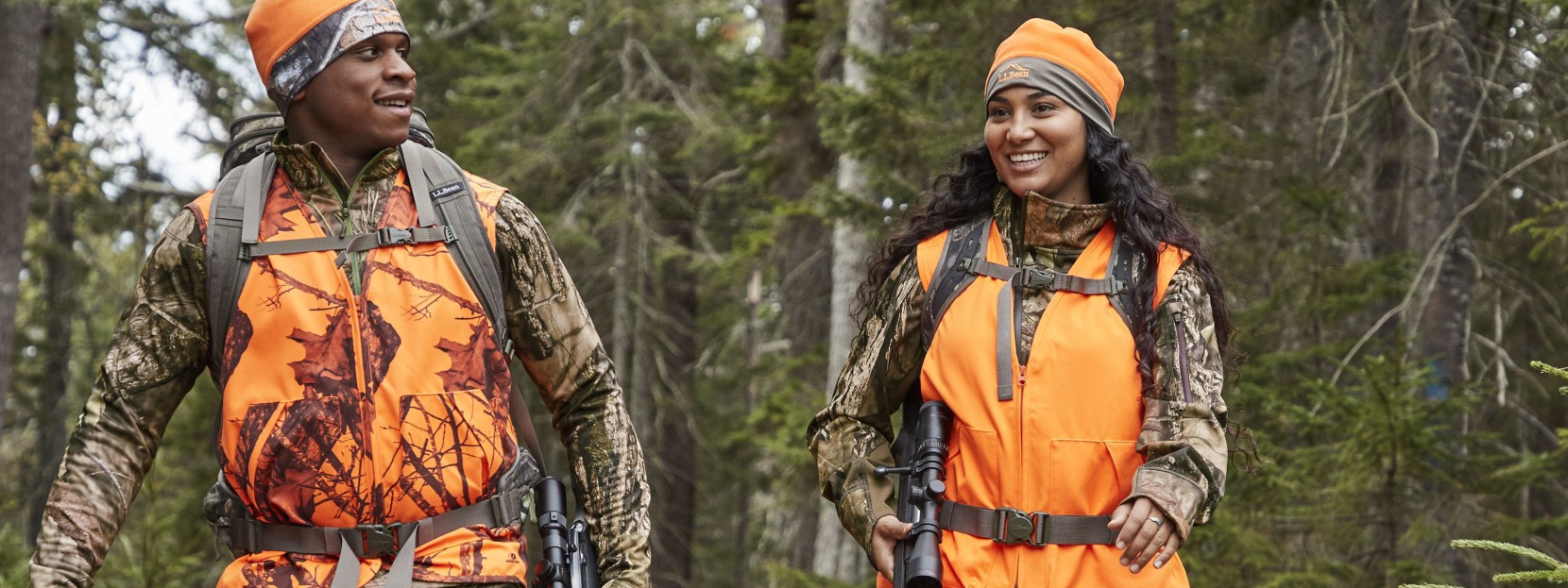 Man and woman wearing hi-vis orange hunting vests walking in the woods.
