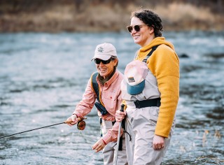 Julie M. standing in a stream being coached by her fly-fishing instructor.