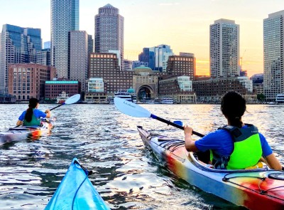 3 kayakers approaching Boston Harbor at sunset.