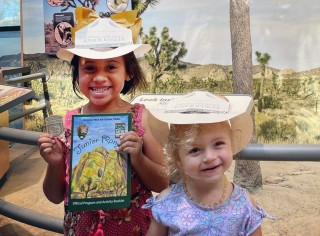 Smiling children holding a Joshua Tree Junior Ranger booklet.