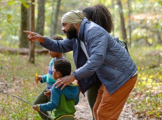 A family pauses on their walk in the woods to look where Dad is pointing.