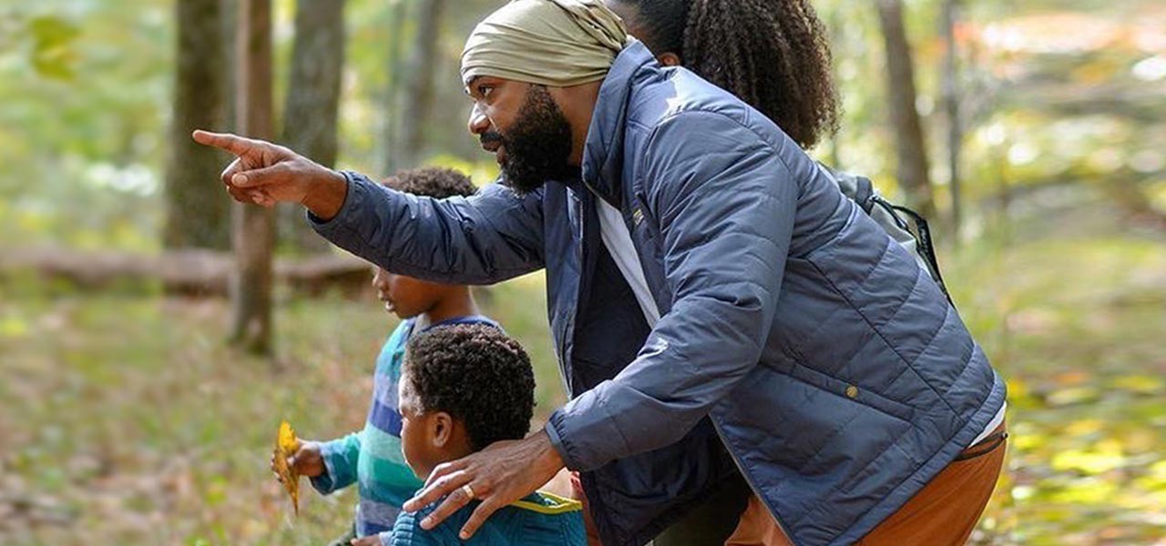 A family pauses on their walk in the woods to look where Dad is pointing.