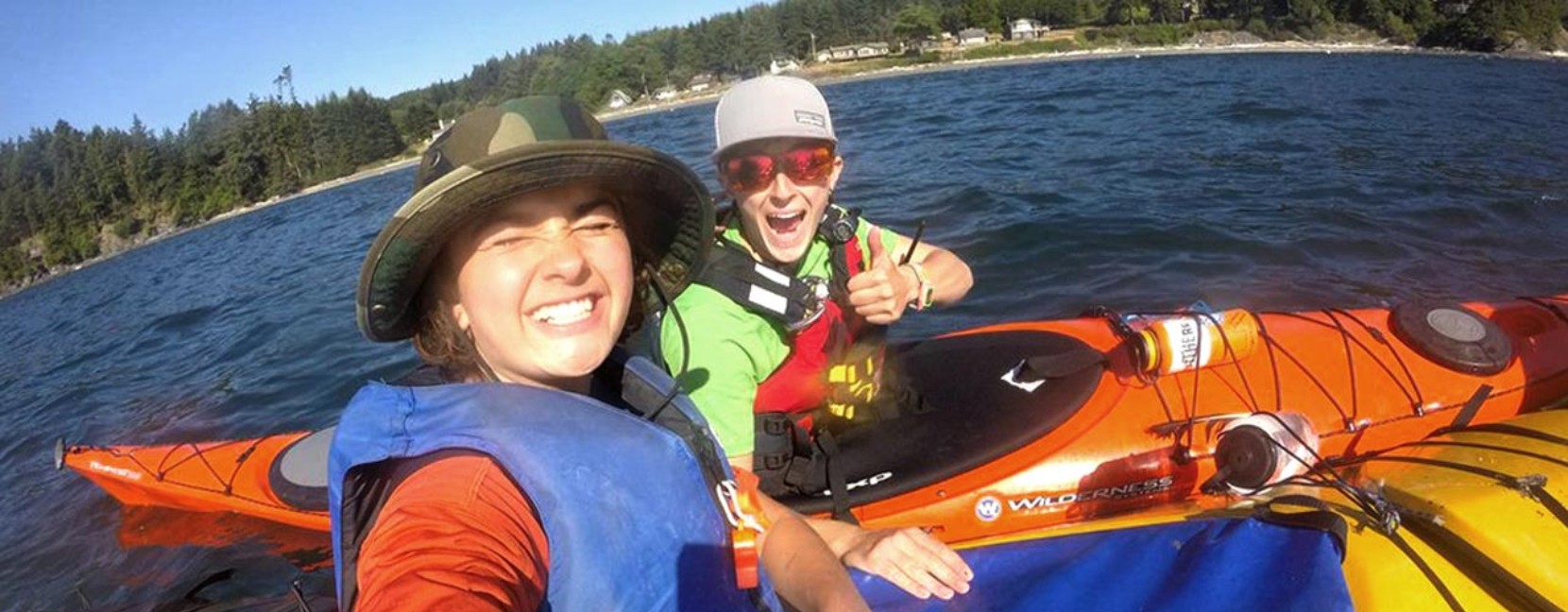 Two women in kayaks pose for a selfie with big grins.