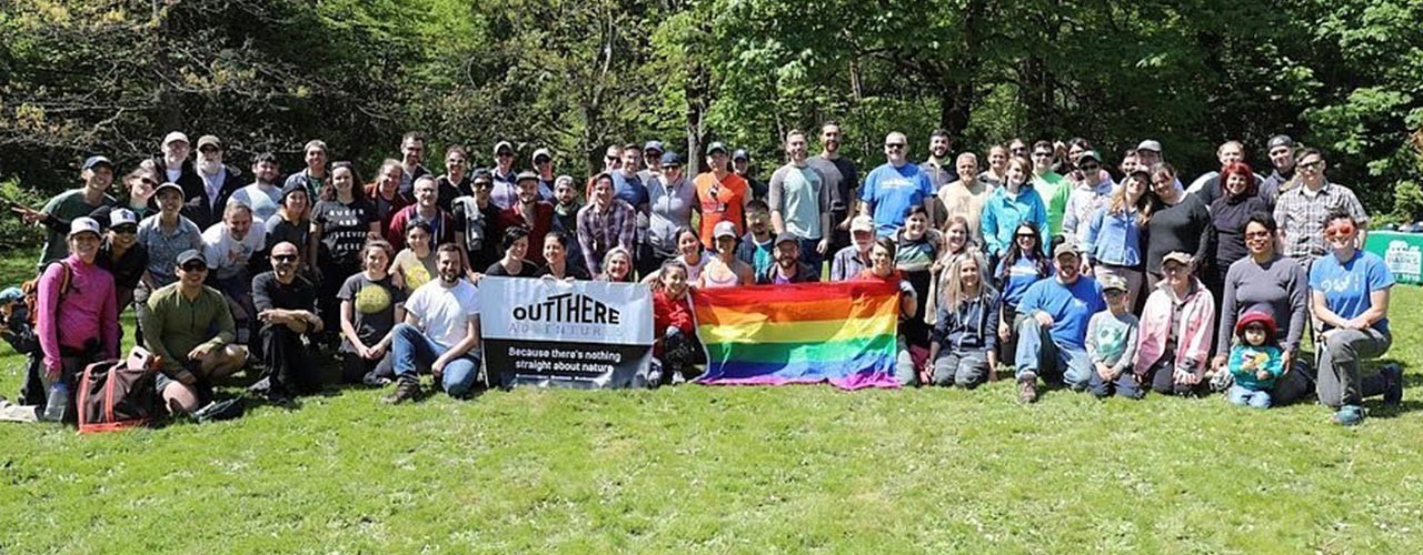 Approximately 80 people posing for a group shot with OUT There Adventures and rainbow banners.