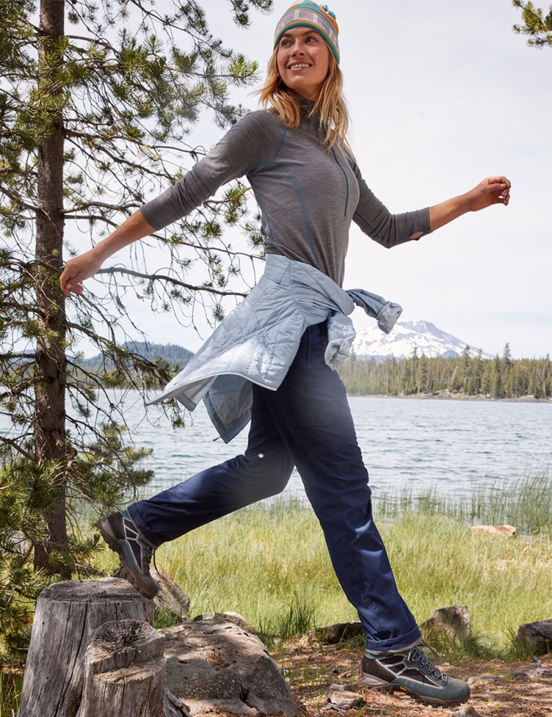 A woman hiking by the water, a lightweight jacket tied around her waist.