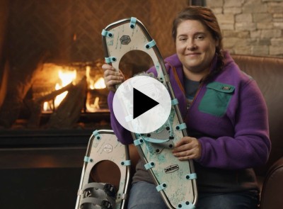 MacKenzie holding a snowshoe in front of a fireplace.