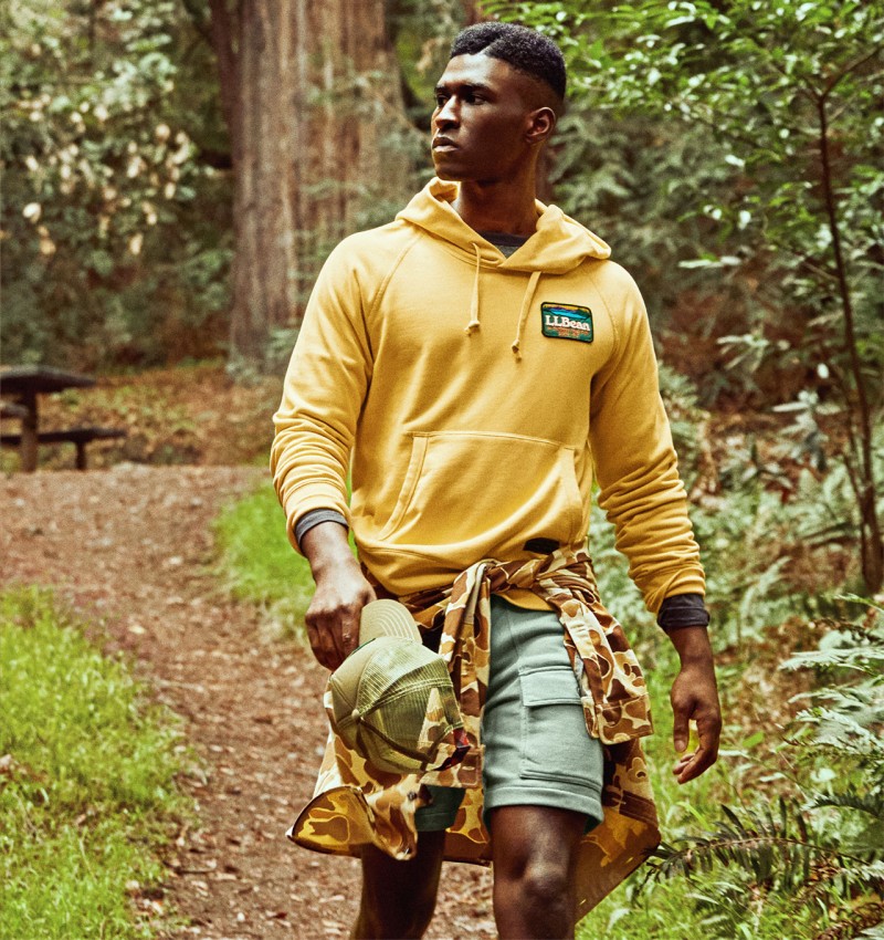 Man walking in woods wearing yellow hooded sweatshirt with L.L.Bean logo on chest.