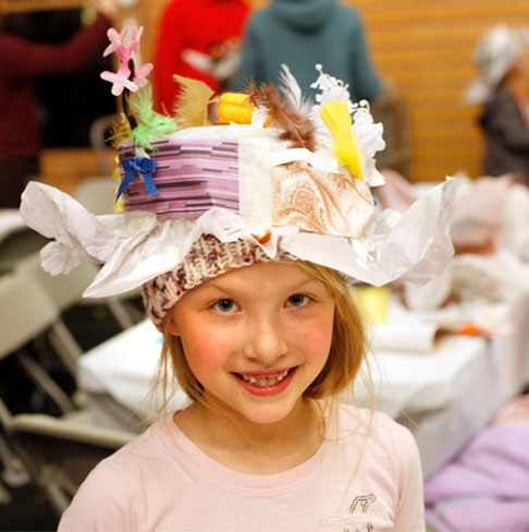 A young girl wearing a fun handmade paper hat.