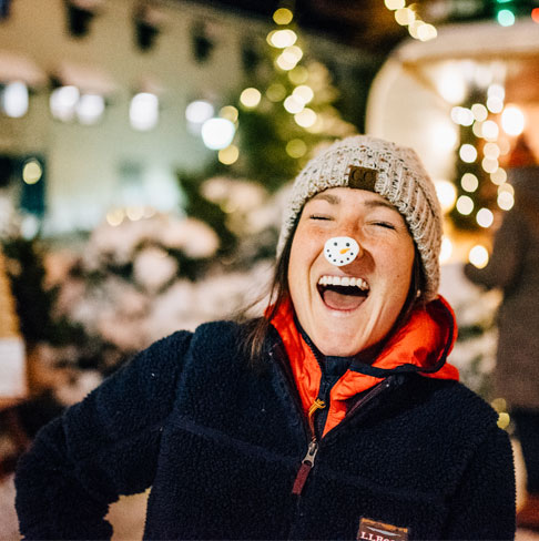 A woman laughing with a snowman sticker on her nose.