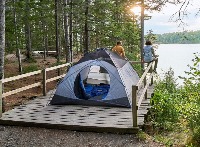 Couple sitting on a fence overlooking the water, a pitched tent behind them.