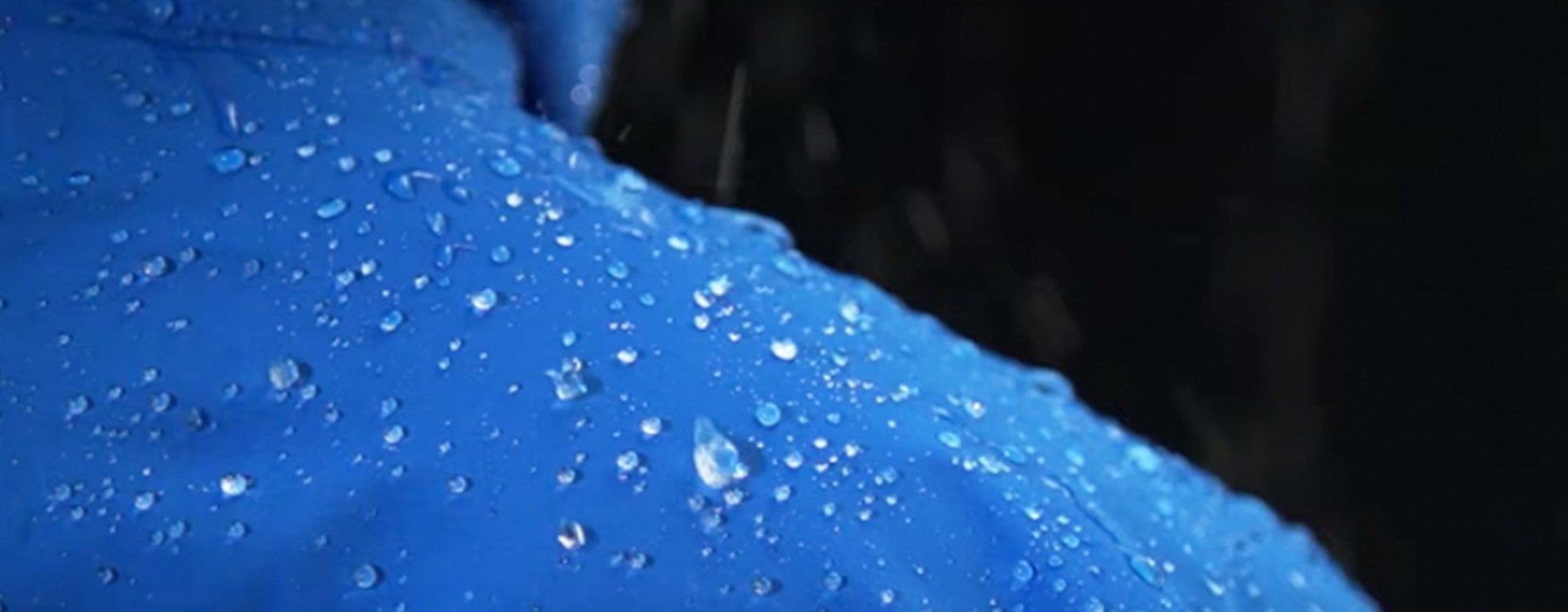 The shoulder of a waterproof jacket with water droplets beading on it.