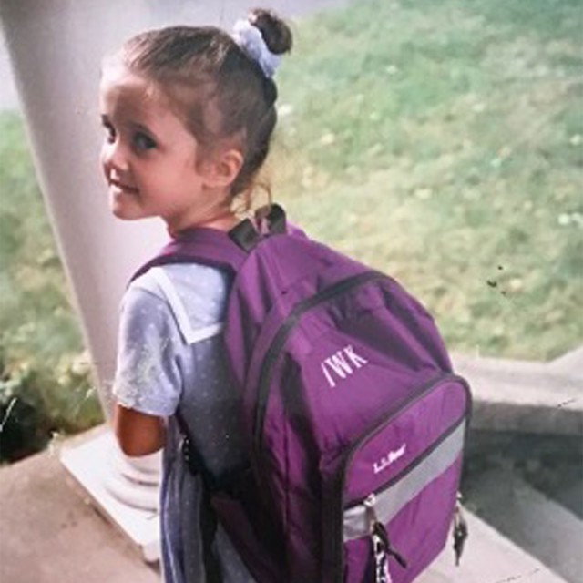 A cute young girl with a purple, monogrammed L.L.Bean backpack.