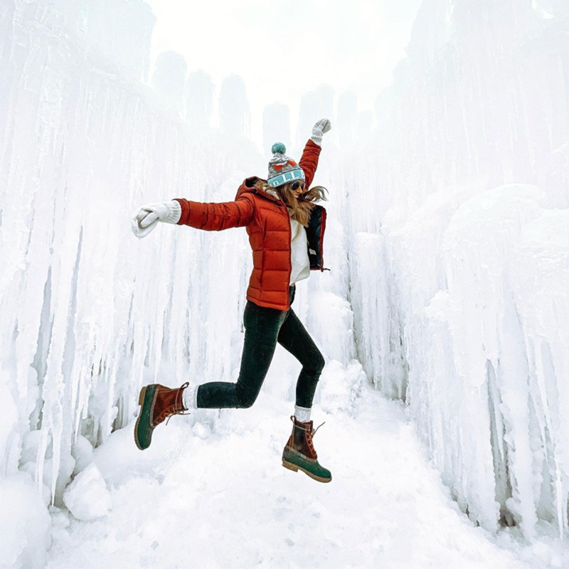 A woman joyfully leaping outdoors in winter among giant icicles.