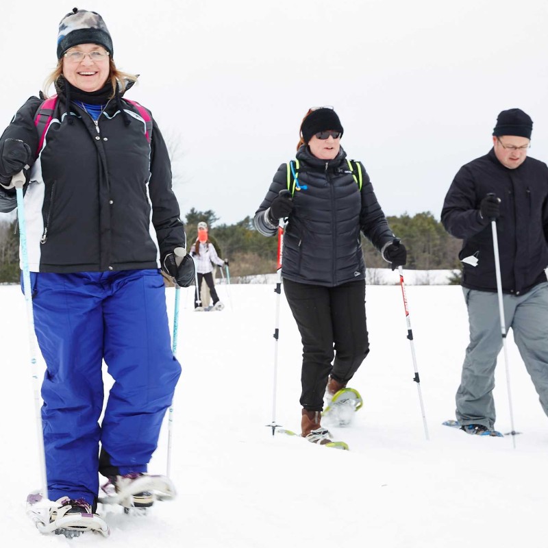 A group of people snowshoeing wearing backpacks and using poles.