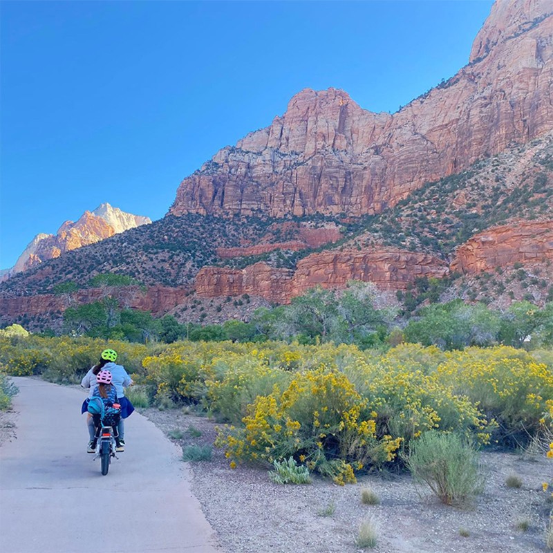 Melody Forsyth and daughter on a bicycle riding on a path alongside chiseled mountains.