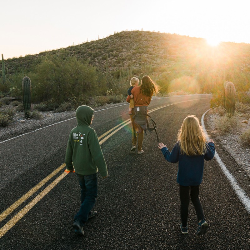 Madison Bowman and kids walk on a road in a desert, the sun dipping below a hill in the distance.