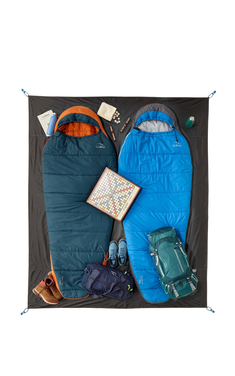 An overhead shot of 2 sleeping bags arranged on a 3-person tent footprint, all extra gear inside the footprint.