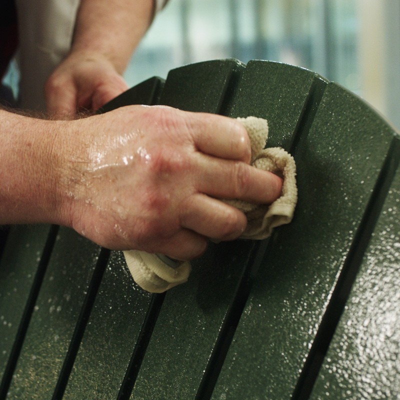 Close-up of a hand with a wet towel washing the back of an adirondack chair.