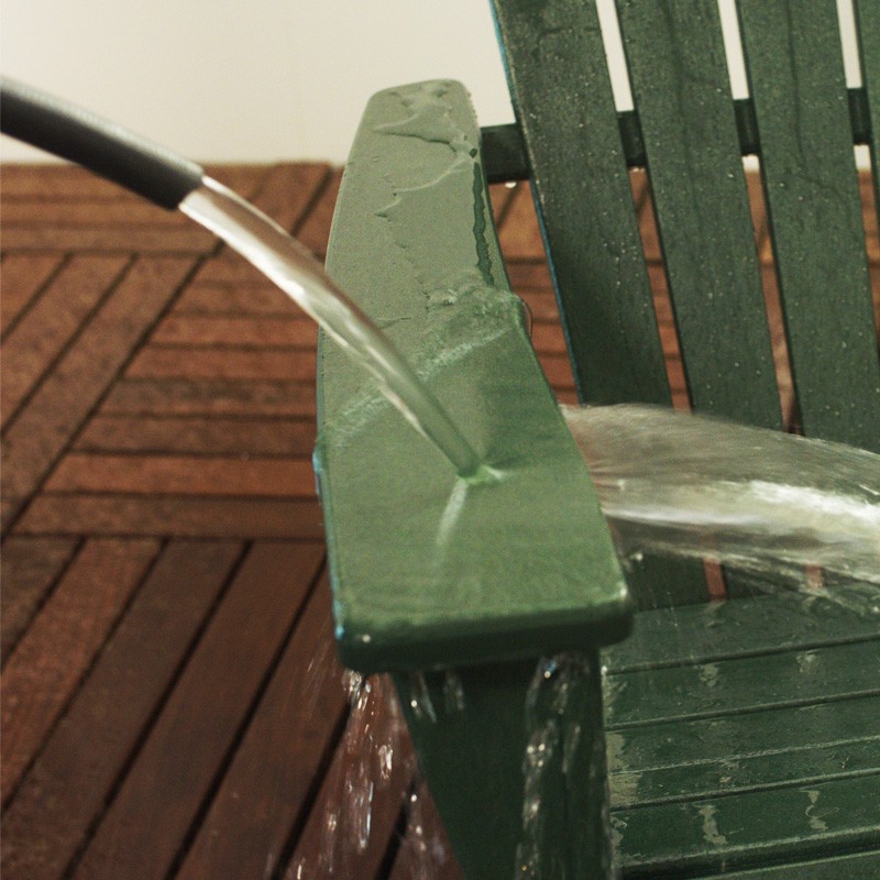 Close-up of the end of a hose directing water on the arm of an adirondack chair.