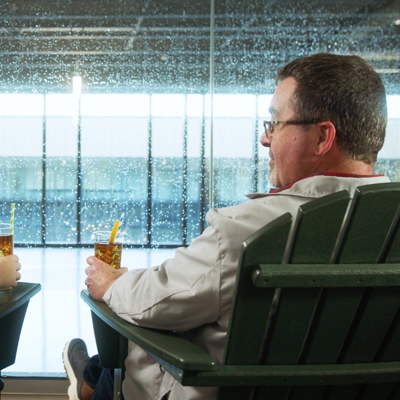 A man sitting in a clean adirondack chair with a glass of iced tea.